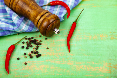 Peppercorns, pepper mill, chili and a towel on a green wooden background.の写真素材