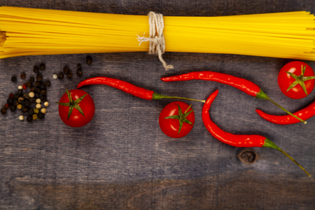 Spaghetti on a dark wooden background. Raw pasta,tomatoes and chili close-up.の写真素材