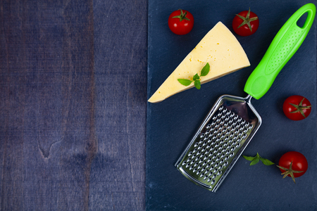 Cheese, cherry tomatoes, basil and grater on a dark background.の写真素材