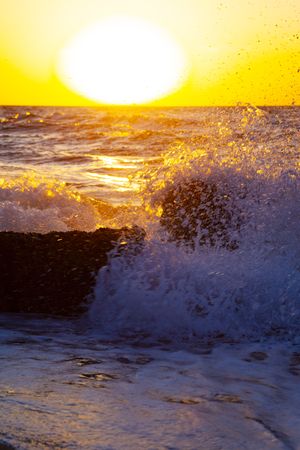 Beautiful sea at sunset. Spray and stone against the background of the yellow sun. Seascape.の写真素材