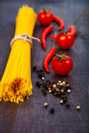 Spaghetti on a dark wooden background. Raw pasta,tomatoes and chili close-up.の写真素材
