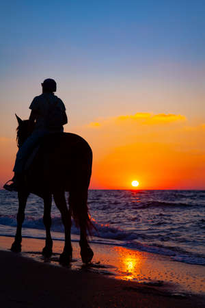 Woman riding a horse on the beach at sunset.の写真素材