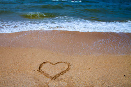 Beautiful beach and sea surf. Summer seascape. Heart in the sand and wave close up.の写真素材