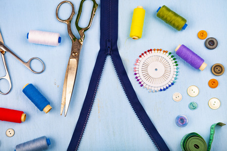 Unbuttoned zipper and sewing accessories on a blue wooden background. Measuring tape, pins, buttons, zipper, scissors and thread.の写真素材