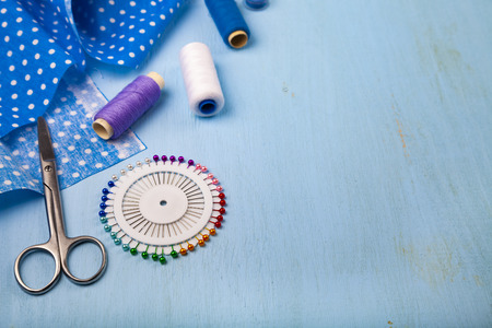 Sewing accessories on a blue wooden background. Blue fabric, scissors and thread.