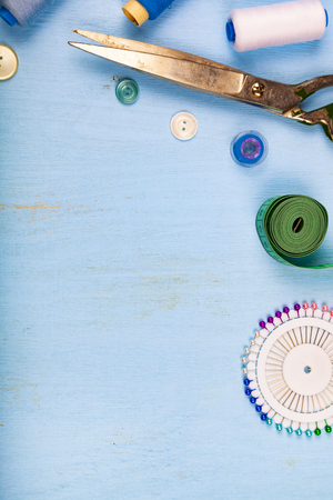Sewing accessories on a blue wooden background. Measuring tape, pins, buttons, zipper, scissors and thread.の写真素材
