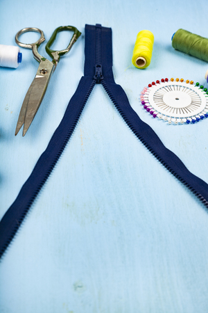 Unbuttoned zipper and sewing accessories on a blue wooden background. Measuring tape, pins, buttons, zipper, scissors and thread.の写真素材