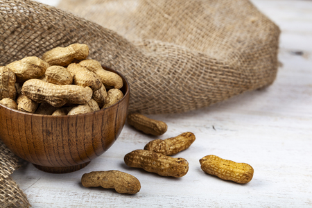 Peanuts in a wooden bowl and burlap on the table. Delicious and healthy nuts.