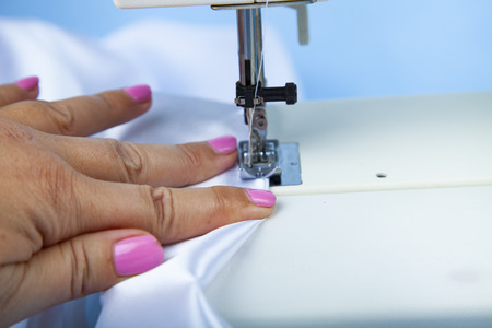 Woman sews on a sewing machine.Sewing machine and white satin fabric close-up