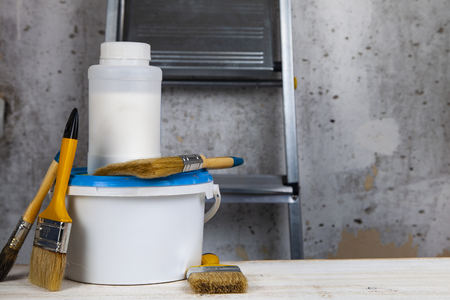 Paint can,roller and brush on the table. Items for home or office renovation against a gray wall and ladder.の写真素材