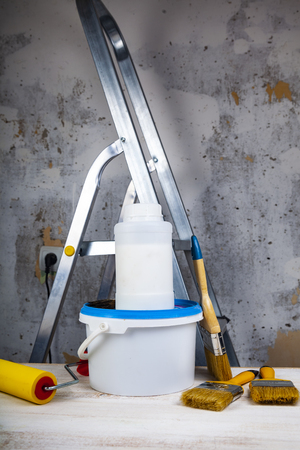 Paint can,roller and brush on the table. Items for home or office renovation against a gray wall and ladder.の写真素材