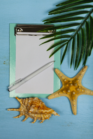 Planning a trip to the sea. Paper,seashells, starfish and leaf of palm tree on a blue wooden background.の写真素材