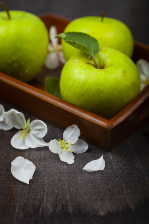 Green apples, flowers and leaves on a wooden tray. Still life with fruit on a wooden table.の写真素材