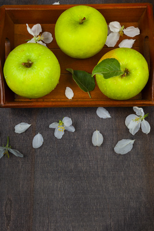 Green apples, flowers and leaves on a wooden tray, top view. Still life with fruit on a wooden table.の写真素材