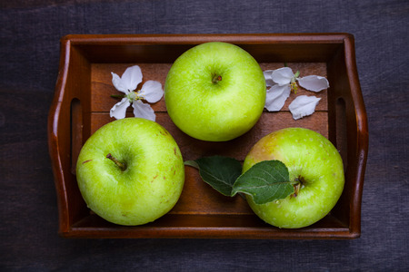 Green apples, flowers and leaves on a wooden tray, top view. Still life with fruit on a wooden table.の写真素材