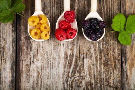 Ripe red and yellow raspberries and blackberries in spoons on an old wooden table. Delicious berries.の写真素材