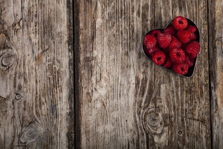 Ripe raspberries in the shape of a heart on an old wooden table. Delicious berries.の写真素材