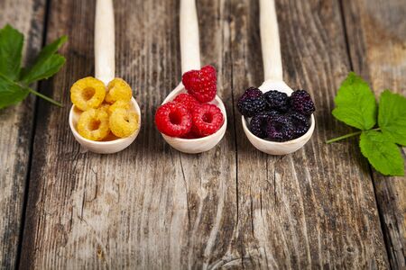 Ripe red and yellow raspberries and blackberries in spoons on an old wooden table. Delicious berries.の写真素材