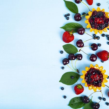 Small berry cake and ripe berries on a blue wooden background. Delicious dessert. Place for your text.の写真素材