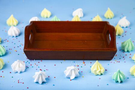 Meringue and a wooden tray on a blue background. Delicious dessert. Colorful handmade meringue.