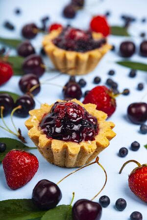 Small berry cake and ripe berries on a blue wooden background. Delicious dessert.の写真素材