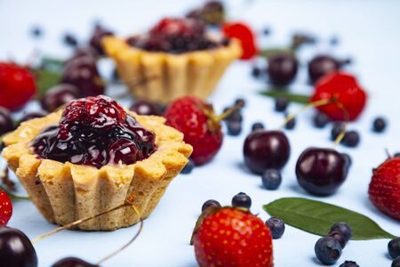 Small berry cake and ripe berries on a blue wooden background. Delicious dessert.の写真素材