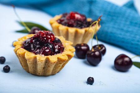 Small berry cake and ripe berries on a blue wooden background. Delicious dessert.の写真素材
