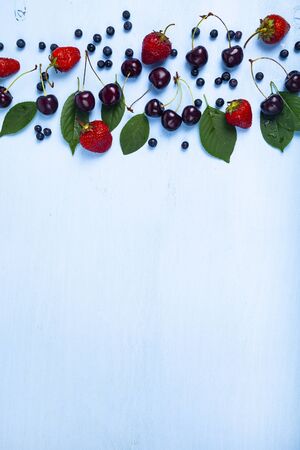 Ripe berries on a blue wooden background. Blueberries, cherries and strawberries close-up. Place for your text.の写真素材