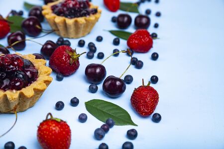 Small berry cake and ripe berries on a blue wooden background. Delicious dessert.の写真素材