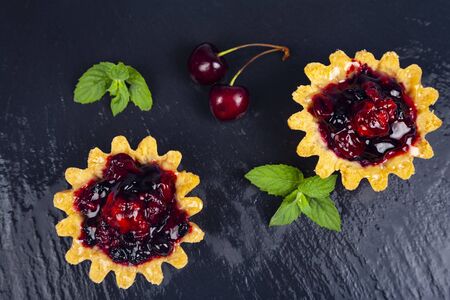 Small berry cake, sweet cherry, blueberry and mint on a black slate tray, top view. Delicious dessert.の写真素材