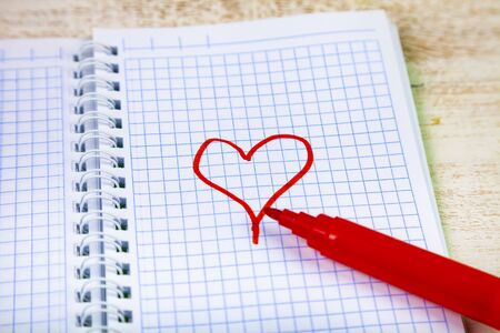 Felt pens and notebook. Red heart is drawn on a checkered sheet.