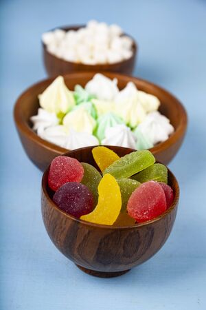 Meringue,marmalade and marshmallow in wooden bowls on a blue background. Delicious dessert.の写真素材