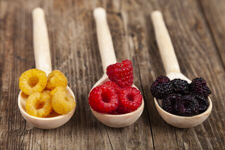 Ripe red and yellow raspberries and blackberries in spoons on an old wooden table. Delicious berries.の写真素材