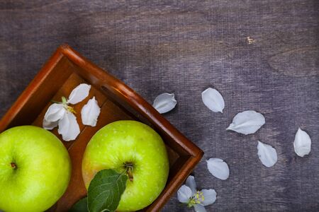 Green apples, flowers and leaves on a wooden tray. Still life with fruit on a wooden table.