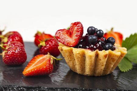 Small berry cake and strawberries on a dark background. Delicious dessert.