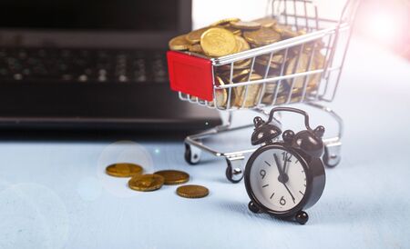 Business still life. Laptop, shopping cart with coins and watch on a blue table.の写真素材