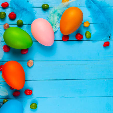 Eggs, candies and feathers on a blue wooden background, place for your text. Easter still life.