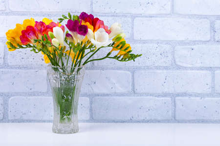 Bouquet of multi-colored freesias in a crystal vase on a brick wall background. Beautiful flowers.の写真素材