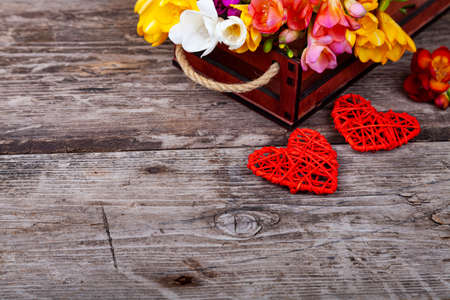 Multicolored freesia in a box and two hearts on an old wooden background. Beautiful flowers.Place for your text.の写真素材