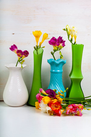 Beautiful flowers. Freesias in multi-colored vases on a white wooden background.の写真素材