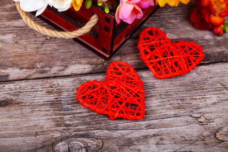 Multicolored freesia in a box and two hearts on an old wooden background. Beautiful flowers.