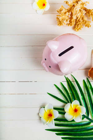 Pig piggy bank, palm leaf and seashells on a wooden background, top view. Concept: saving for vacation.の写真素材