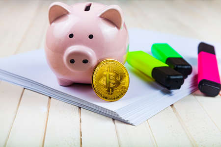Pig piggy bank, colored markers and bitcoin on a white wooden background.
