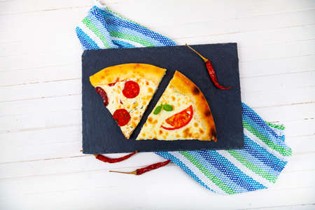 Two slices of pizza on a black serving board. Delicious food on a wooden background.の素材 [FY310169569722]