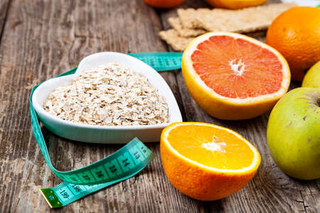 Useful products, measuring tape, oatmeal and dumbbells on a wooden background. Diet and healthy lifestyle.の写真素材
