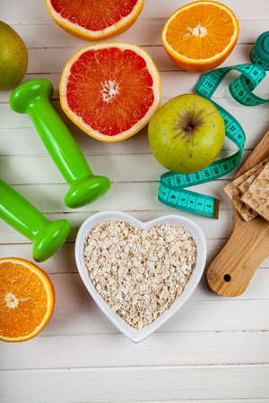Useful products, measuring tape, oatmeal and dumbbells on a wooden background. Diet and healthy...