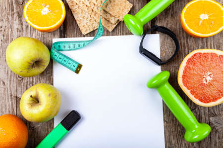 Useful products, measuring tape, fitness bracelet and dumbbells on a wooden background. Diet and healthy lifestyle.の写真素材