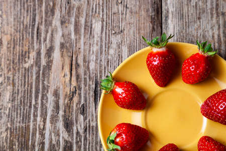 Ripe strawberries in a yellow plate on a wooden background.の写真素材