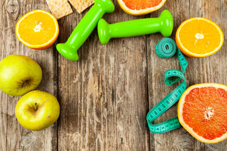 Useful products, measuring tape, oatmeal and dumbbells on a wooden background. Diet and healthy lifestyle.の写真素材