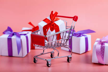 Shopping cart and gifts on a pink background. Concept: buying gifts.の写真素材